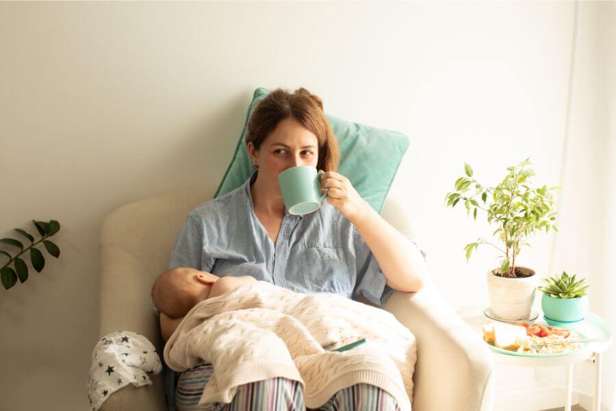 Maman en train de boire dans une tasse à la maternité en tenant bébé dans les bras.